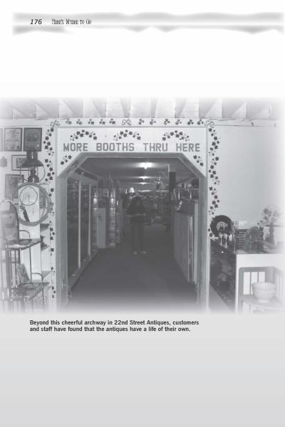 Black-and-white photo from Scare-izona by Schiffer Publishing, Ltd.: an archway in an alleged haunted Arizona antique shop, with a "MORE BOOTHS THRU HERE" sign, shelves of vintage items, and a person at the entrance to another room.