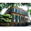 Featured in "Savannah Perspectives" by Schiffer Publishing, Ltd., a historic two-story house with green shutters and a white balcony stands in Savannah, Georgia, marked as a notable city landmark.