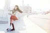 A woman with long dark hair and tattoos, wearing a red skirt and black top, smiles by a street pole in LA—an image capturing the spirit of AOI Ink Nymphs Los Angeles by Schiffer Publishing, Ltd., perfect for tattooed model features.