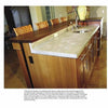 A kitchen island with Schiffer Publishing, Ltd.’s Cast-in-Place Concrete Countertops features an undermount sink, dark wood cabinets, and wicker-backed chairs. A large vase sits on the counter, with a dining area visible in the background.