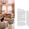 A living room styled with patterned furniture, green curtains, wall art, and a black-and-white rescue dog on a round ottoman, as featured in "At Home with Dogs" by Schiffer Publishing, Ltd.; the right page shows the article "So Much Love.