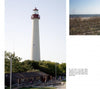 A tall white lighthouse with a red top rises behind trees and a wooden building, near a sandy beach. "Cape May Perspectives" by Schiffer Publishing, Ltd. explores the Cape May lighthouse and its links to Victorian architecture.