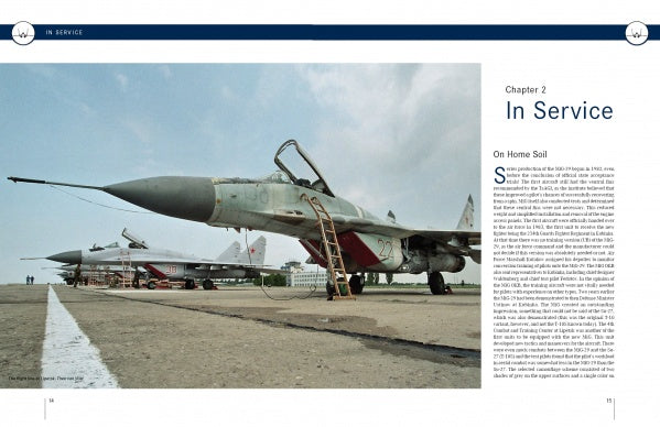 Two MiG-29 air-superiority fighters, featured in "The MiG-29" by Schiffer Publishing, Ltd., are parked on an airfield under a clear sky, with a building and trees visible in the distance. One fighter stands in the foreground and another in the background.