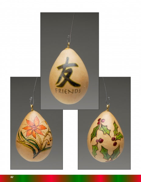 Three egg-shaped gourd ornaments from "Making More Gourd Ornaments" by Schiffer Publishing, Ltd. hang against a gray background, featuring FRIENDS with a Chinese character, a red flower with leaves, and holly—perfect for festive decor.