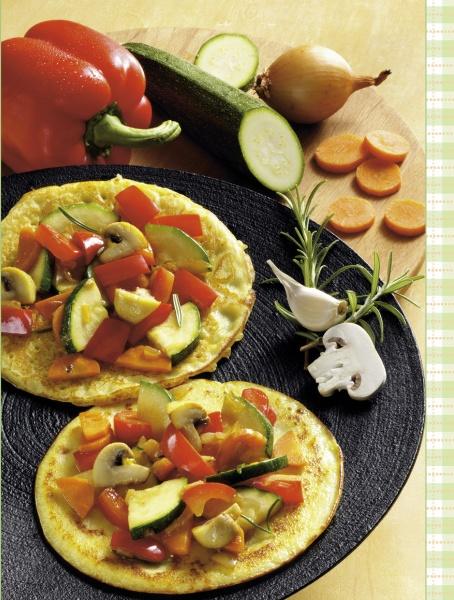 Two omelets with sautéed vegetables, including zucchini, are presented on a black plate surrounded by fresh veggies—perfect inspiration from Schiffer Publishing, Ltd.'s Squash & Zucchini. Fresh vegetables adorn the wooden surface around the plate.