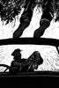 A black-and-white illustration from "Scary Urban Legends" by Schiffer Publishing, Ltd. shows a frightened woman and man in a car, staring up at two feet in fishnet stockings hanging ominously above them, evoking tense classic urban legend vibes.