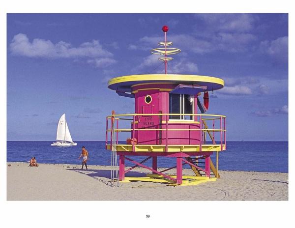 South Beach Lifeguard Stations by Schiffer Publishing, Ltd. features a vivid pink and yellow lifeguard stand on sandy Miami Beach near the ocean, with a sailboat on the water and a person walking under a blue sky.