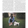 A man in blue kneels on grass, petting two white setters, with a white house and trees behind him. Featured: "The Real Ryman Setter: A History with Stories from the Appalachian Grouse Covers" by Schiffer Publishing, Ltd.