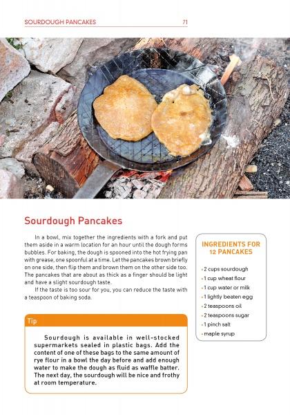 Two pancakes cook in a black grill pan over an outdoor wood fire, as shown in the book "On an Open Fire" by Schiffer Publishing, Ltd. A sourdough pancake recipe and a yellow ingredients box appear below the image.