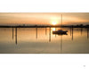 A small sailboat rests on calm water at sunset near Martha’s Vineyard, its reflection shimmering, as captured in "Martha’s Vineyard Wide" by Schiffer Publishing, Ltd., with warm light and wooden posts completing the tranquil scene.