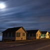 Cape Cod Nights by Schiffer Publishing, Ltd. captures small seaside cabins along a quiet road beneath a cloudy, moonlit sky, evoking the peaceful charm of Cape Cod nights with soft moonlight shimmering on the ocean.