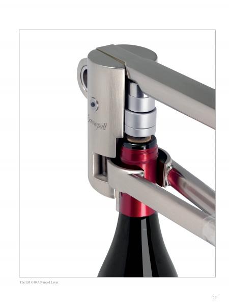 A close-up of the Screwpull corkscrew by Schiffer Publishing, Ltd. shows its lever mechanism uncorking a red wine bottle, with the opener attached securely to the bottle’s neck.