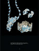 The Margot Van Voorhies set by Schiffer Publishing, Ltd. features mid-century-inspired blue and white chrysanthemum designs on a necklace, bracelet, ring, and earrings, all elegantly displayed on a black background.