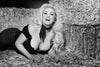 A woman with long, wavy blonde hair poses playfully on hay, smiling in this striking black-and-white photo by Marilee Caruso, featured in "Modern Vintage Pin-Up" from Schiffer Publishing, Ltd.