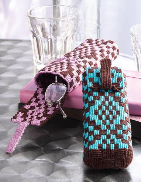 Two pairs of eyeglasses in colorful Knot Design cases by Schiffer Publishing, Ltd.—one pink and brown, one turquoise and brown—rest on a closed pink notebook beside clear glasses on a silver textured surface.