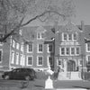 Black and white photo of a historic brick building with windows and central stairs. A car and person with dog out front. Caption: The Belvoir Winery in Liberty, featured in Campfire Tales Midwest by Schiffer Publishing, Ltd.