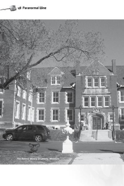 Black and white photo of a historic brick building with windows and central stairs. A car and person with dog out front. Caption: The Belvoir Winery in Liberty, featured in Campfire Tales Midwest by Schiffer Publishing, Ltd.