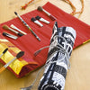 A red fabric brush holder with paintbrushes lies open on a wooden surface next to a rolled-up brush holder featuring a black-and-white cityscape patchwork, crafted using techniques from "Free-Form Patchwork Techniques" by Schiffer Publishing, Ltd.