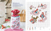 A drawstring bag with Véronique Enginger’s Little Red Riding Hood cross stitch from Schiffer Publishing, Ltd.’s "Fables & Fairy Tales to Cross Stitch" sits on a table beside flowers, mushrooms, and the matching pattern chart.