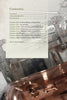 A page from Coulter & Payne Farm Distillery's 101 Uses for Moonshine by Schiffer Publishing, Ltd. shows the table of contents over a grayscale image of a copper still, with chapters on moonshine history, social skills, recipes, and farm-to-bottle trends.