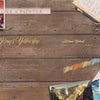 A wooden table with watercolor art supplies, finished paintings, brushes, a floral plate, and handwritten notes. Text reads The Painter's Wedding by Schiffer Publishing, Ltd., with tips and techniques for wedding painting inspiration.
