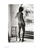 Inspired by Vivienne Maricevic, "She Shoots Men" by Schiffer Publishing, Ltd. features black and white male nude photography—a nude man indoors by a wooden stool, gazing through an open door at sunlit patio plants in an intimate moment.