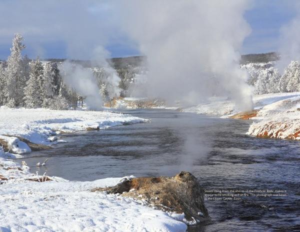 Experience Yellowstone National Park with Schiffer Publishing, Ltd.: snow blankets the landscape as a river winds past steaming geysers and snow-covered trees beneath a clear sky.