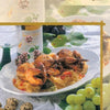 A plate of roasted quail, featured in "Cooking Wild Game" by Schiffer Publishing, Ltd., rests on vegetables and herbs, surrounded by green grapes, quail eggs, a wine glass, and a bottle atop a white tablecloth.