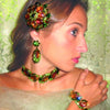 A woman wearing vibrant jewelry featured in "The Art of Juliana Jewelry" by Schiffer Publishing, Ltd.—with ornate green and orange gemstones—poses against a lacy, light green background.