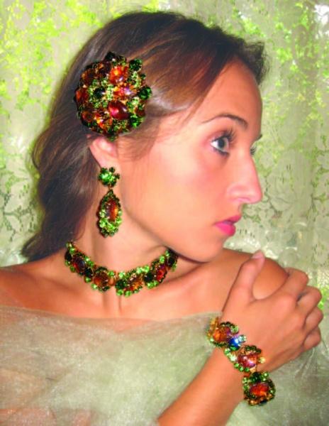 A woman wearing vibrant jewelry featured in "The Art of Juliana Jewelry" by Schiffer Publishing, Ltd.—with ornate green and orange gemstones—poses against a lacy, light green background.