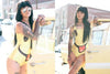 A woman with long dark hair, sunglasses, and tattoos poses by a yellow car in a smiley-face swimsuit, channeling the SoCal vibe of tattooed models featured in "AOI Ink Nymphs Los Angeles" by Schiffer Publishing, Ltd.