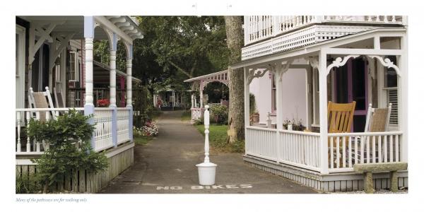 A quiet, tree-lined path in Oak Bluffs runs between white houses with porches and flowers—a perfect scene captured in "Oak Bluffs on the Vineyard" by Schiffer Publishing, Ltd., ideal for any Martha’s Vineyard souvenir book.