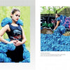 A woman in a sleeveless black top and striking blue ruffled fiber art gown poses near graffiti outdoors, fabric spread around her, as seen in Schiffer Publishing, Ltd.'s "Artistry in Fiber, Vol. 3." A text profile is shown on the left page.