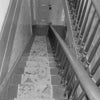 Black-and-white photo of a narrow, carpeted stairwell with wooden handrails, leading to a closed door. Text reads "Piercing the Veil," a book from Schiffer Publishing, Ltd., featuring the haunted Whaley House of San Diego.