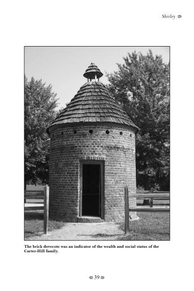 A round brick dovecote with a conical shingled roof stands amid grass and trees, ringed by a wooden fence. Its open doorway recalls the eerie stories found in "Haunted Plantations of Virginia" from Schiffer Publishing, Ltd.