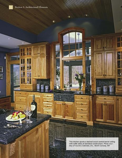 A spacious kitchen features elegant cabinets, black granite counters, a large arched window, and a barrel ceiling. An island set for two displays cake, fruit, wine—showcasing design tips from The Kitchen Guide by Schiffer Publishing, Ltd.