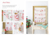 The Magic of Christmas to Cross Stitch" by Schiffer Publishing, Ltd. is featured in a wooden frame with embroidered pockets inspired by cross-stitch patterns, set on a rustic table decorated for Christmas.