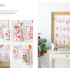 The Magic of Christmas to Cross Stitch" by Schiffer Publishing, Ltd. is featured in a wooden frame with embroidered pockets inspired by cross-stitch patterns, set on a rustic table decorated for Christmas.