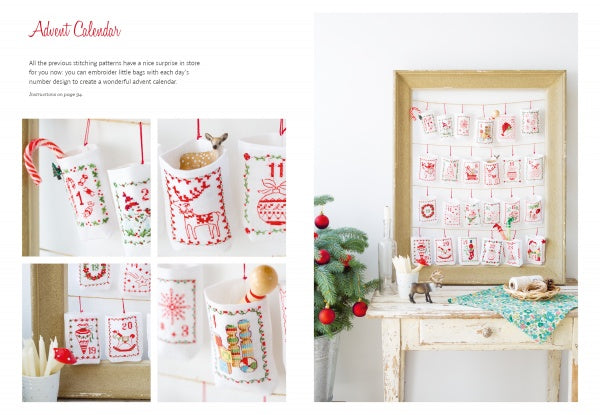 The Magic of Christmas to Cross Stitch" by Schiffer Publishing, Ltd. is featured in a wooden frame with embroidered pockets inspired by cross-stitch patterns, set on a rustic table decorated for Christmas.