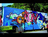 Truck Art by Schiffer Publishing, Ltd. showcases a blue-based trailer adorned with vibrant graffiti of bold shapes and letters in pink, orange, green, and blue, parked outdoors near trees and gravel.
