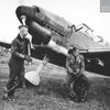 Two WWII-era pilots pose by a Bf 109 on a grassy airfield, recalling the Legion Condor’s role in the Spanish Civil War, as explored in "German Eagles in Spanish Skies" from Schiffer Publishing, Ltd.