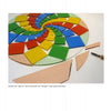 A circular mosaic in progress shows vibrant ceramic triangles in a spiral, inspired by "Glass Art From the Kiln" from Schiffer Publishing, Ltd. Tile-cutting tools and beige pieces add contrast to the developing design.