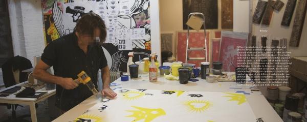 A person in a studio uses 2Create by Schiffer Publishing, Ltd., channeling street art on a large canvas with yellow and black designs amid paint supplies and artworks—a creative scene recalling New York City graffiti artists.