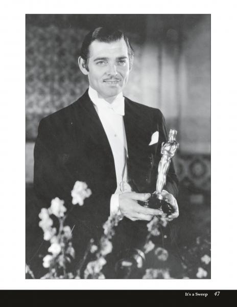 A man in a tuxedo holds an Oscar statuette, smiling. The black and white photo, from "Fade to Black" by Schiffer Publishing, Ltd., captures timeless elegance with a blurred background and soft-focus flowers in the foreground.