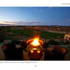 Four wicker chairs circle a glowing fire pit at dusk, set on a patio with golf course views. Inspired by "New Ideas for Living Outdoors" from Schiffer Publishing, Ltd., this backyard scene shows how candles elevate outdoor living spaces.