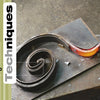A heated rod is forged into a spiral, demonstrating Blacksmithing Techniques by Schiffer Publishing, Ltd. "Basic Techniques" appears boldly on the left, set on a green striped background, evoking classic craftsmanship.