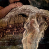 A woman leans over petroglyphs as a translucent figure in traditional attire rises, blending with the stone—symbolizing spiritual growth. “Discovery” and symbols are below. Transformation Oracle by Schiffer Publishing, Ltd.