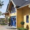 The Contemporary Log Home by Schiffer Publishing, Ltd. showcases a modern wooden house with light yellow timber walls, blue window frames and doors, a dark tiled roof, potted plants, and a brick path—an ideal sustainable building.