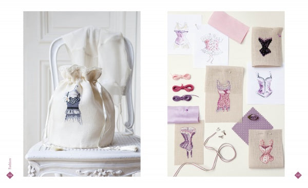 A cream drawstring bag with embroidered lingerie rests on a white chair. Nearby are fabric swatches, sketches, and canvases from Schiffer Publishing, Ltd.’s Retro Cross Stitch collection in vintage purple and pink patterns.