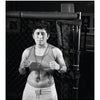 A person with short hair and a cross necklace stands in front of a chain-link fence, embodying the fierce spirit of classic fighter portraits, as featured in "Tough Guys" by Schiffer Publishing, Ltd.